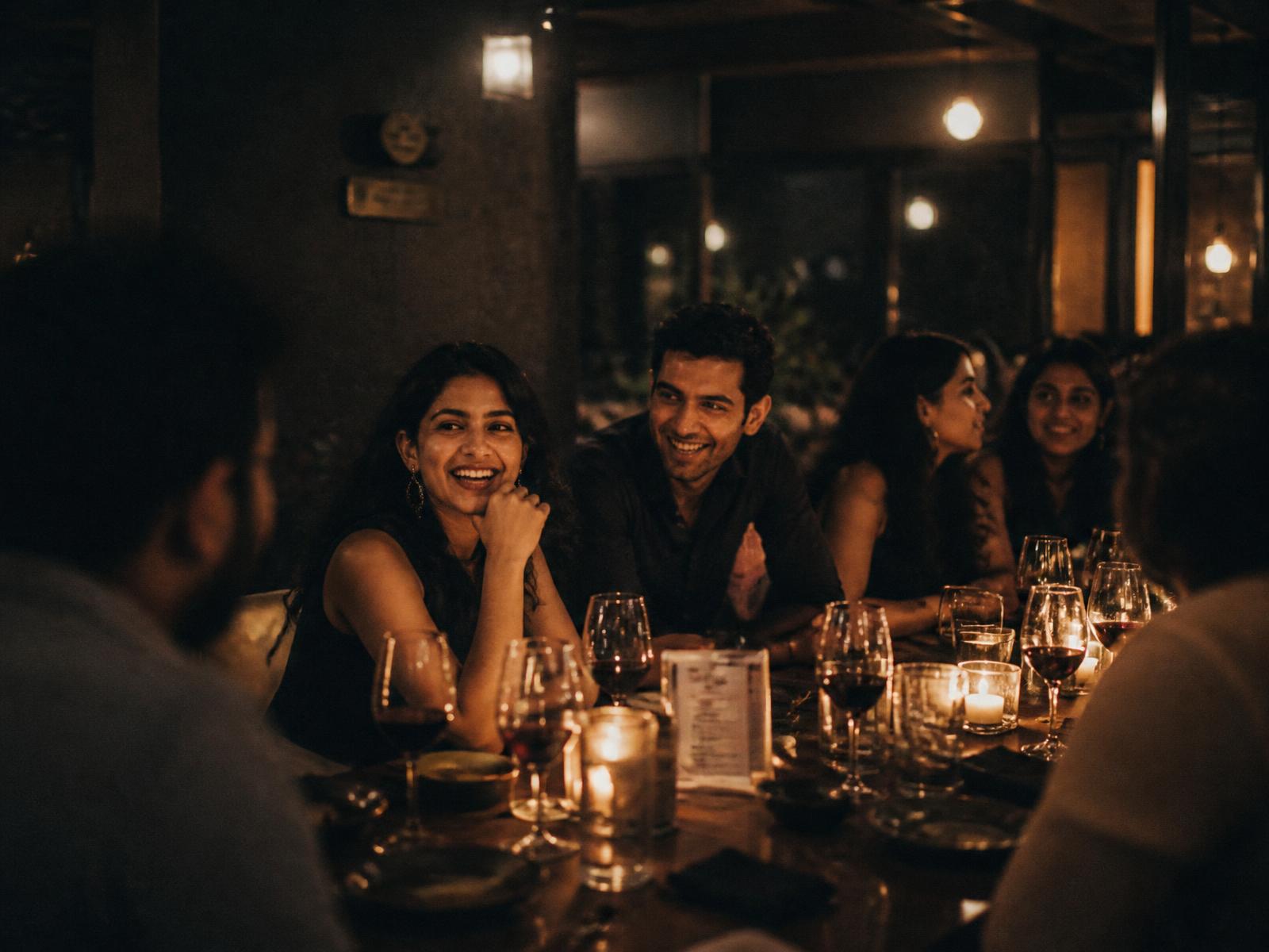 A group of young people talking and laughing around a candlelit dinner table in Bangalore